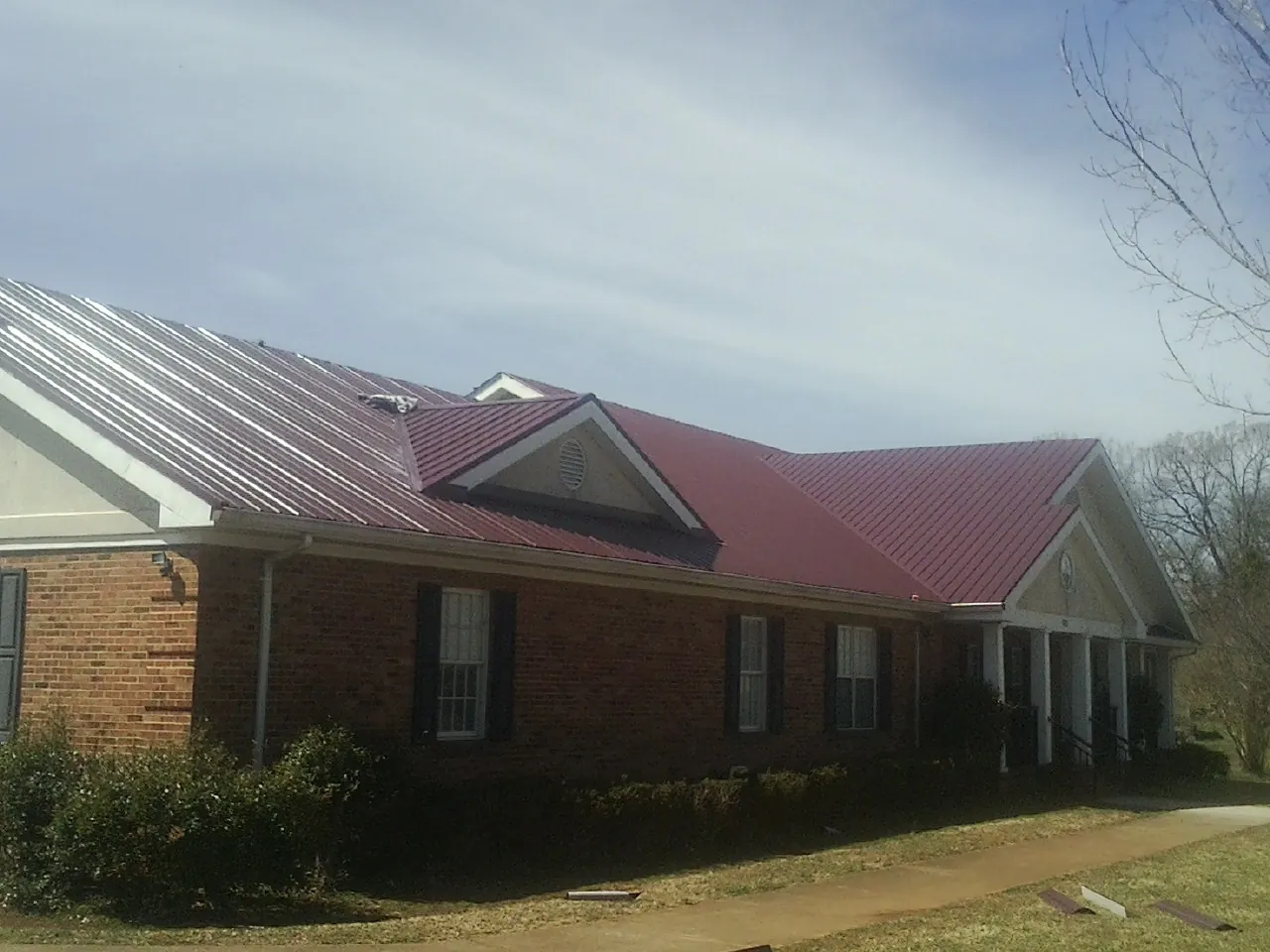 Red metal roof with gabled entries on a long brick building, from a Hail Damage Roof Repair job in Sisseton