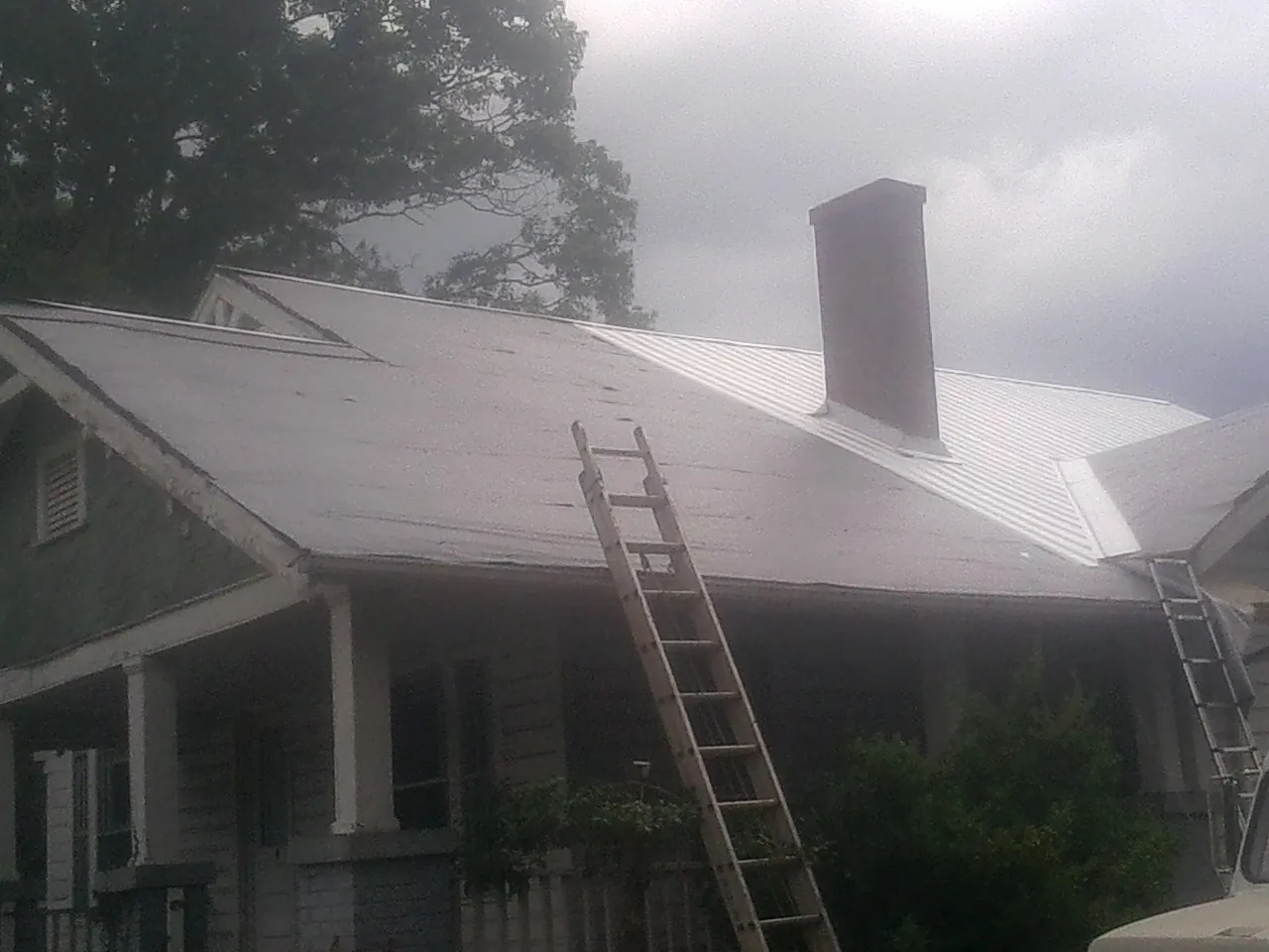 Ladders against a metal roof on an older home with a brick chimney in Sisseton