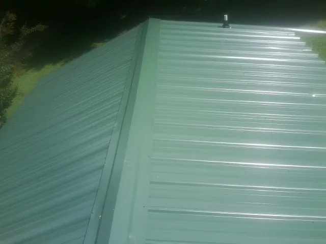 New green metal panels meeting at the ridge of a roof — Flat Roof Repair work by our crew in Sisseton