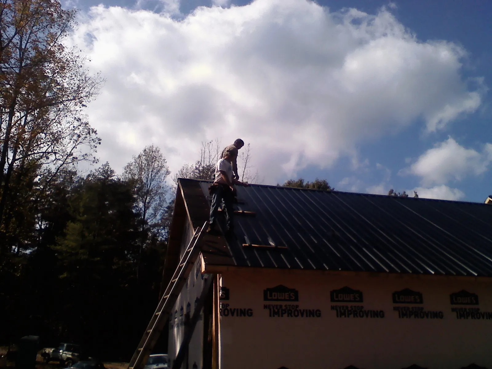 Roofer fastening dark metal panels high against a cloudy sky, from a Roof Inspection job in Sisseton